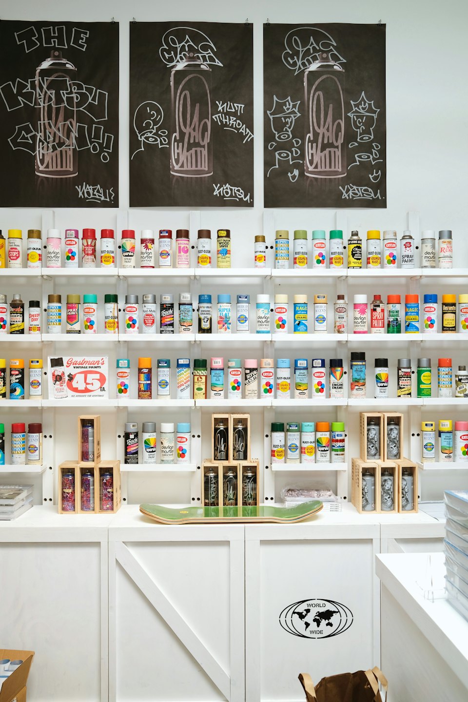 Colorful spray paint cans displayed on white shelves with graffiti art posters.