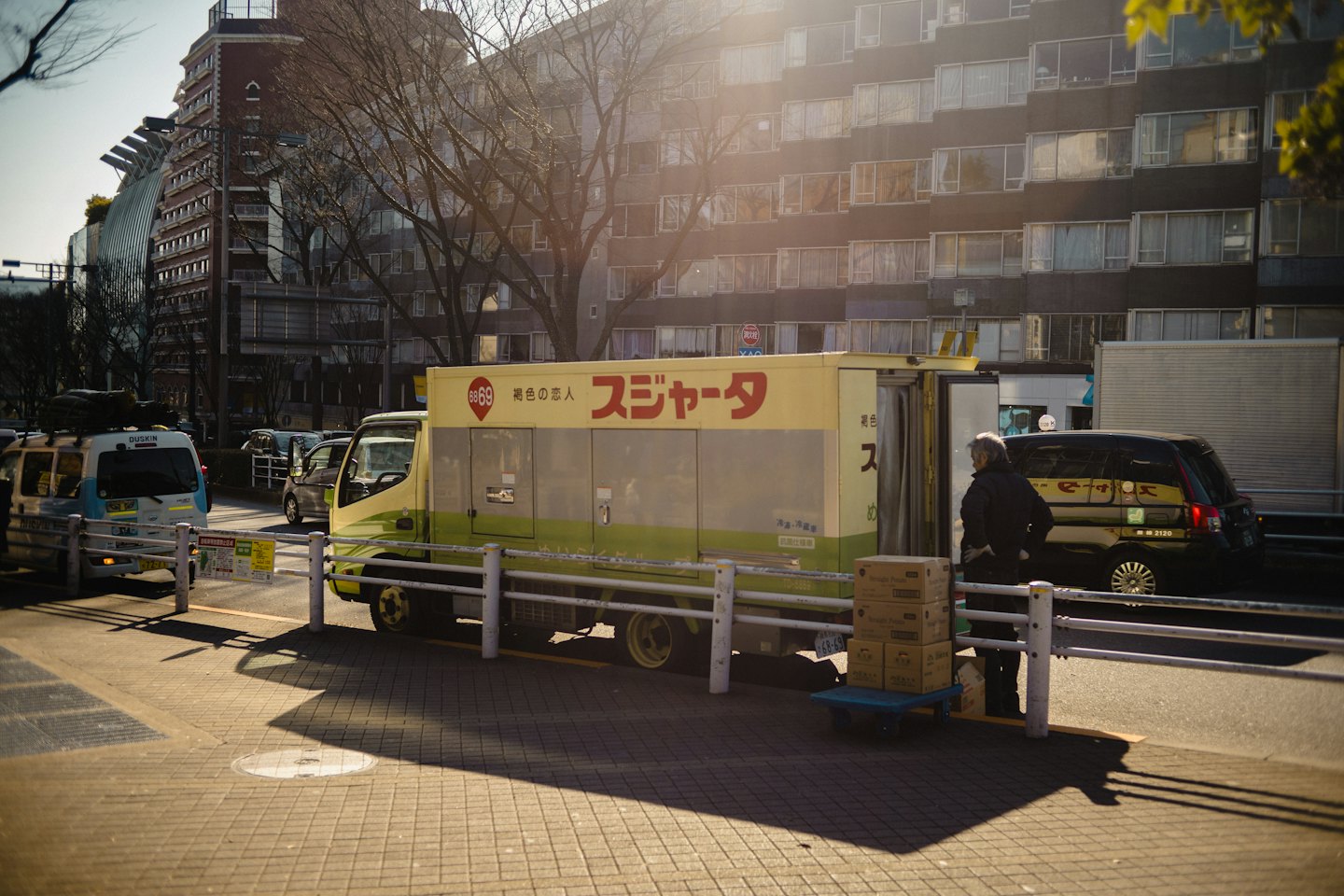 Delivery worker stands with packages by a yellow and green truck.